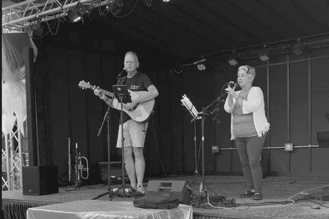 Lela and Dennis Whalen performing on stage with guitar and microphones